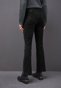 Pantaloni neri a zampa d'elefante con un motivo a stampa leopardata, realizzati in un tessuto testurizzato. Abbinati a stivali neri alla caviglia con un accento dorato.