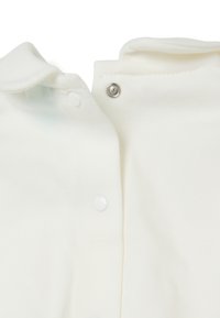 Weißes Kleidungsstück mit rundem Kragen, ausgestattet mit Druckknöpfen und weicher, glatter Textur. Das Design beinhaltet subtile Stickdetails.