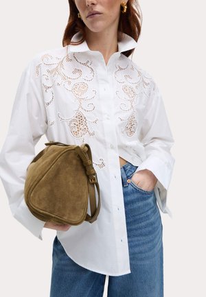 Witte blouse met laser-geknipte ontwerpen, gecombineerd met een bruine suède handtas. De outfit bevat wijde jeans en gouden accent oorbellen.