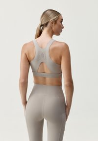 Soutien-gorge de sport beige avec un dos ouvert et des perforations, associé à un legging taille haute assorti. Texture lisse et coupe ajustée.