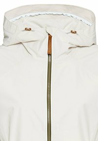 Helle beige wasserfeste Jacke mit hohem Kragen, verstellbarem Kapuzenaufsatz und einem kontrastierenden grünen Reißverschluss. Strukturierter Stoff mit glatten Akzenten.