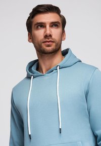 Felpa leggera blu con cappuccio, caratterizzata da un cordino, corde bianche a contrasto, una tasca frontale e un tessuto morbido e testurizzato. Design semplice e vestibilità rilassata.