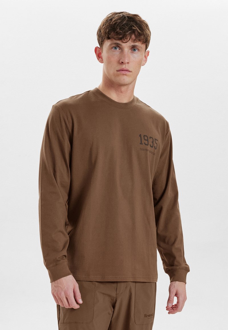 Camicia marrone a maniche lunghe in cotone, caratterizzata da un collo tondo e una grafica frontale con l'anno "1935" in stampa scura. Design semplice, vestibilità comoda.