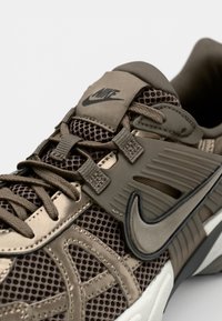 Nike Sneaker mit einem oberen Teil aus beige-braunem Mesh, kontrastierenden Lederelementen, strukturierten Überzügen und einem auffälligen Logo auf der Zunge.