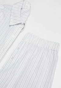 Vitt pyjamas-set som består av en knapp-up topp med blå ränder och ett par byxor med elastisk midja med matchande ränder. Mjuk tygtextur.