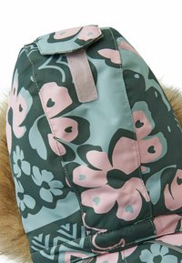 Tessuto con motivo floreale in tonalità di verde e rosa. Presenta un accento in pelliccia, dettagli di cucitura e una chiusura in velcro nella parte superiore.