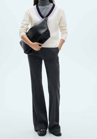Pull en maille blanc avec un col en V et une bordure violette, assorti à un pantalon évasé gris foncé et une grande pochette noire. Texture lisse.