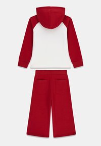 Roter und weißer Hoodie mit roter Kapuze und Ärmeln, kombiniert mit roten, weit geschnittenen Jogginghosen mit zwei Gesäßtaschen. Weiche Stoffstruktur.