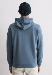 Kapuzensweatshirt aus hellblauem Stoff, mit geripptem unteren Saum und Bündchen. Kombiniert mit einer dunkel gestrickten Mütze. Rückansicht zeigt eine glatte Textur.