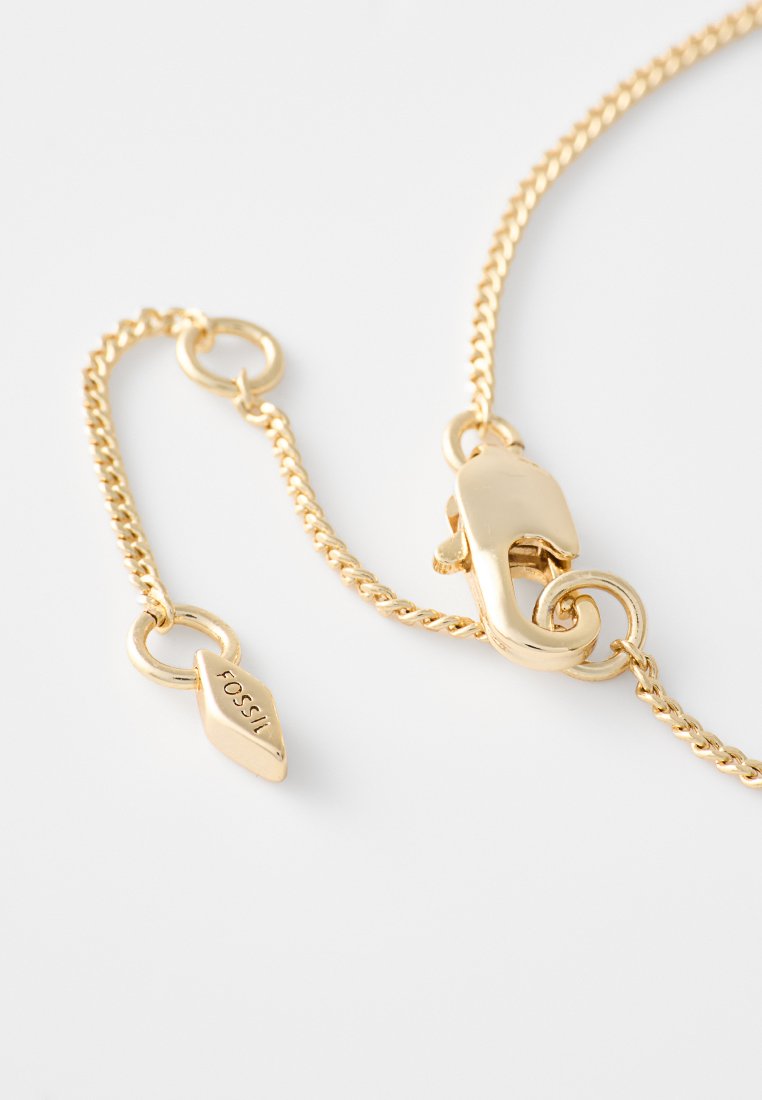 Goldfarbene Metallkette mit einem Karabinerverschluss und polierter Oberfläche. Enthält einen herabhängenden Anhänger mit eingraviertem "Fossil".