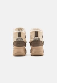 Beige en bruine winterlaarzen met zachte bontvoering, textiel- en suède materialen, gevoerde kraag en gestructureerd detail van hardware aan de achterkant.