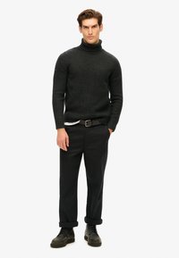 Suéter de punto de cuello alto gris oscuro, de corte ajustado, con puños acanalados, combinado con pantalones negros y zapatos oscuros, que presentan puños enrollados y un cinturón de tela.