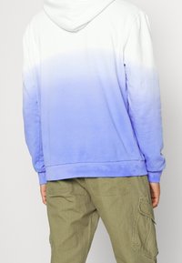 Hooded sweatshirt with white to light blue gradient. Features long sleeves and a relaxed fit, paired with olive green cargo pants.