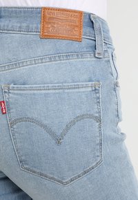 Ljusblå denimjeans med en brun läderlapp, hjärtformad sömnad på bakfickan och en röd etikett nära sidledningen.