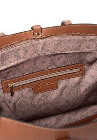 Interior de bolso de cuero marrón medio con un bolsillo con cremallera, forro beige con un patrón geométrico y una etiqueta de la marca cosida.