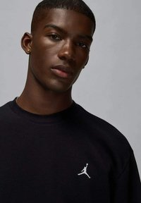 Felpa nera con collo rotondo, con logo Jumpman bianco sul lato sinistro del petto. Tessuto liscio, design minimalista.
