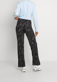 Svarta utsvängda byxor med ett vitt abstrakt mönster, tillverkade av ett lätt tyg, tillsammans med en ljusblå långärmad tröja och vita sneakers.