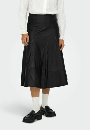 Zwarte leren midi-rok met een uitlopende vorm, zichtbare naden en stikdetails. Gestyled met witte sokken en chunky zwarte schoenen.