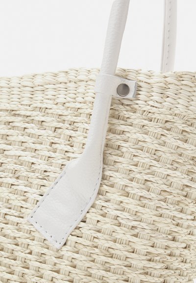 Woven straw bag in off-white with a smooth white leather handle, featuring a circular silver snap detail and textured surface.