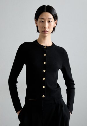 Svart cardigan laget av mykt materiale, med rund halslinning, lange ermer og gullfargede knapper foran.