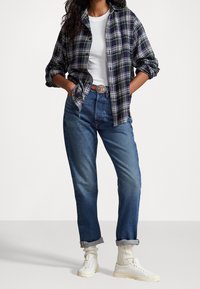 Rutig flanellskjorta i marinblått och grönt, vit t-shirt, högmidjade blå jeans, vita sneakers och krämfärgade strumpor, med uppvikta ärmar.