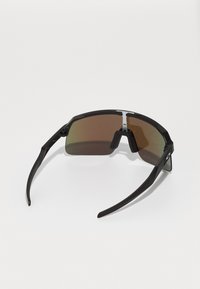 Gafas de sol negras con lentes curvados y de gran tamaño, con tinte en degradado marrón y brazos negros elegantes. Presentan un puente nasal plateado y un Detalle mínimo.