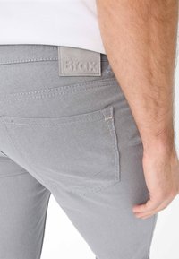 Grau denim Hosen mit strukturiertem Finish, ausgestattet mit einem quadratischen, eingeprägten Brax-Logo an der Taille und standardmäßiger Taschenanordnung.
