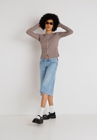Cardigan ribbed de culoare bej deschis cu nasturi la față, asociat cu culottes din denim albastru deschis cu margini desfăcute. Pantofi cu platformă negri și șosete albe.