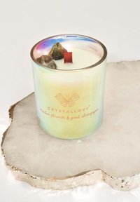 Irydyscentna szklana świeca o zapachu różowego szampana, z czerwoną knotem i dekoracyjnymi kamykami na wierzchu. Złote logo tekstowe u podstawy.