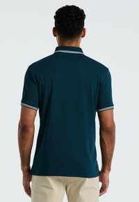 Donkerblauwe polo met een klassieke kraag, korte mouwen met witte strepen en een gladde textuur. Gezien vanuit de achterkant.