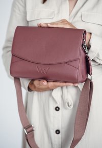 Kleine mauvefarbene Lederhandtasche mit Klappen-Design, verziert mit dezenten Nähten und einem verstellbaren Stoffriemen. Logo präge auf der Vorderseite.