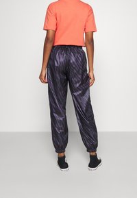 Pantaloni joggers neri e viola con motivo, vita elastica e caviglie strette, abbinati a una maglietta arancione brillante a maniche corte.