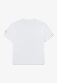 Άσπρη βαμβακερή κοντομάνικη μπλούζα με μικρό κόκκινο λογότυπο τυπωμένο στο αριστερό μανίκι. Απλός σχεδιασμός, κανονική εφαρμογή και λαιμόκοψη στρόγγυλη.