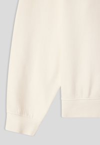 Felpa girocollo in morbido tessuto crema. Presenta polsini e orlo a coste, con una texture liscia e un design minimalista. Nessun motivo o accento.