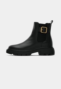 Black leather Chelsea boots featuring a rounded toe, a block heel, and a gold buckle accent on the elastic sides for adjustable fit.