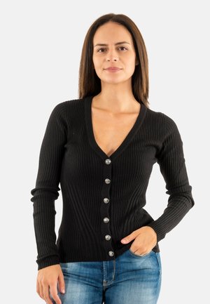 Cardigan nero a coste con scollo a V profondo e chiusura a bottoni argentati, dotato di maniche lunghe e forma aderente, indossato con jeans blu.