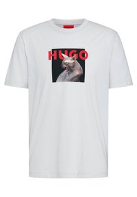 Hvid bomulds t-shirt med et sort firkantet grafisk motiv af en kat med rød "HUGO" tekst ovenover. Korte ærmer og rund hals design.