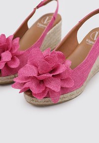 Sandales compensées roses avec un dessus en tissu texturé et un grand accent floral. Un matériau semblable à de la corde naturelle forme le talon compensé.