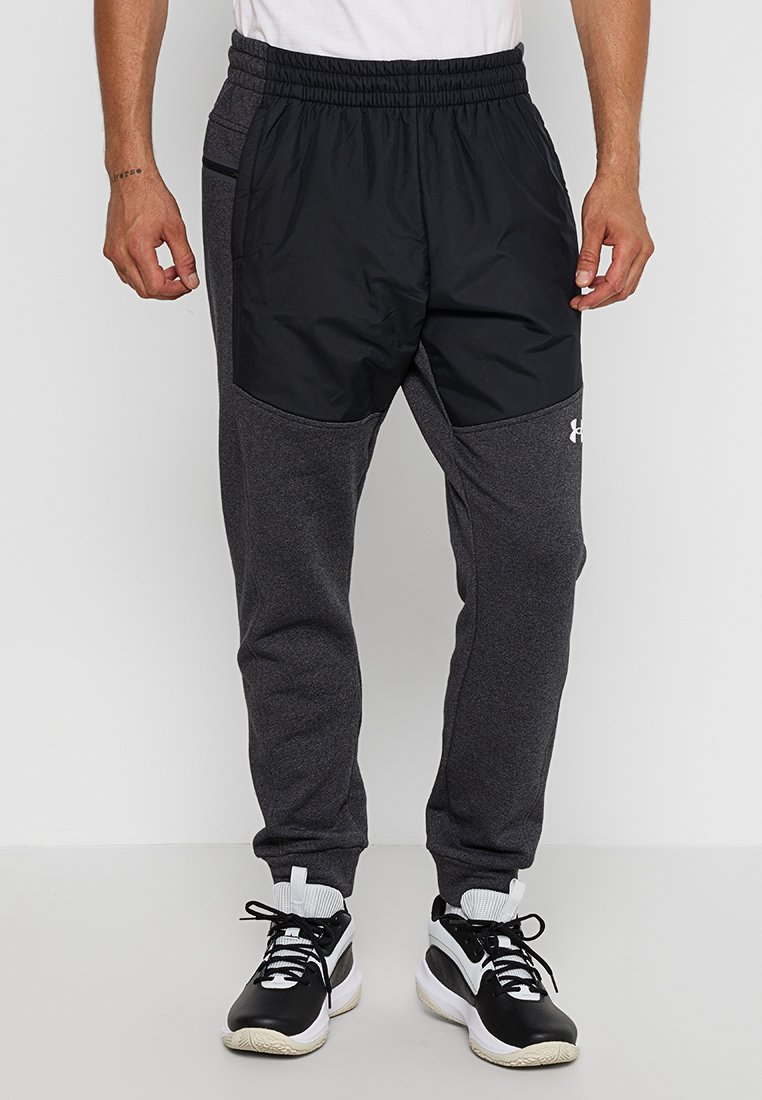 Pantalones de chándal para hombre con parte delantera de nailon negro y parte trasera de forro polar gris oscuro. Presentan una cintura elástica y bolsillos laterales. Combinando con zapatillas negras.