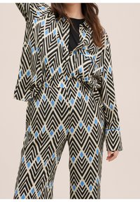 Conjunto de patrones en negro y crema con acentos en azul. El diseño incluye formas geométricas con mangas anchas y pantalones de corte holgado.