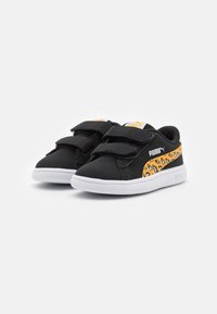 Svarta sneakers med en texturerad finish, med dubbla kardborreband och ett gult leopardmönstrat streck på sidan. Vit gummisula.