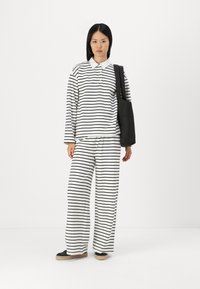 Ensemble de vêtements de détente à rayures noires et blanches comprenant un haut à col et manches longues et un pantalon large. Comprend un sac fourre-tout noir et des chaussures décontractées.