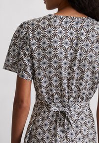 Kurzärmliges Kleid mit geometrischem Muster in Marineblau, Weiß und Gold. Mit taillierter Taille und Bindeband im Rücken.