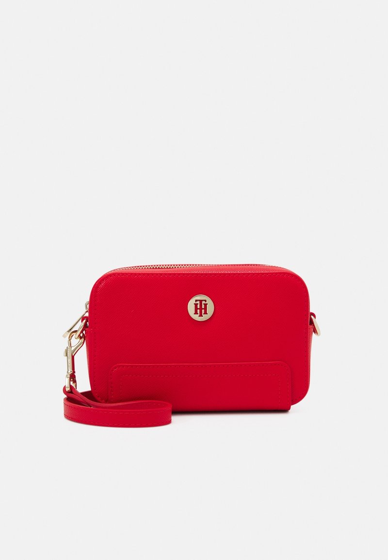 Petit sac de poignet rectangulaire rouge avec fermeture éclair dorée, logo Tommy Hilfiger et bandoulière amovible sur fond blanc.