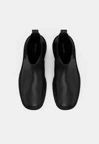 Botas de tornozelo em couro preto com uma textura suave, painéis laterais elásticos, alças de puxar e detalhes costurados ao longo da sola. Marca Calvin Klein no interior.