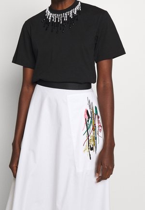 Czarna koszulka z krótkim rękawem z białymi i czarnymi koralikami przy dekolcie, zestawiona z białą spódnicą z kolorowymi, ręcznie wyszywanymi wzorami.