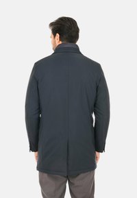 Cappotto blu navy con colletto, spalle strutturate e dettagli delle cuciture visibili. Realizzato in tessuto liscio, presenta un'apertura centrale sul retro.
