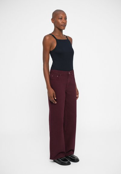 Top negro sin mangas combinado con pantalones burdeos de pierna ancha. Los pantalones tienen bolsillos frontales y acentos metálicos. Modelo lleva zapatos planos negros.