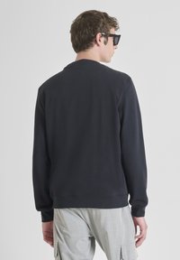 Felpa nera con collo rotondo, tessuto strutturato e polsini a coste. Presenta un logo discreto sul retro, abbinata a pantaloni cargo chiari.