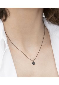 Sort metalhalskæde med en tynd kæde og en lille, cirkulær vedhæng med en struktureret overflade og en lille, farvet sten.